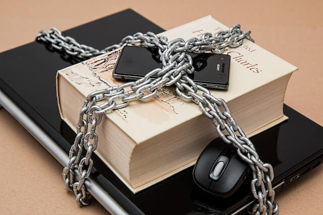 Laptop, Handy und Buch verschlossen. Datenschutz als Hindernis im Arbeitsumfeld